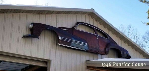 A 1946 pontiac coupe is hanging on the side of a garage.