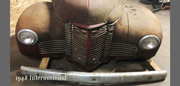 An old rusty car is sitting on a wooden crate in a garage.