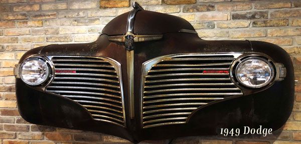 A 1949 dodge car is hanging on a brick wall.