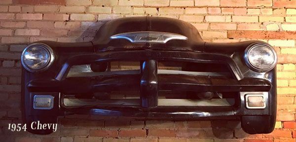 A 1954 chevy is hanging on a brick wall