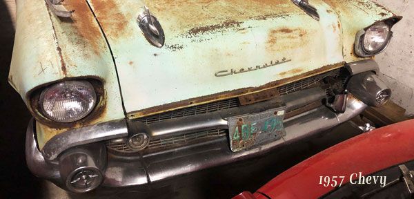 A 1957 chevy is sitting in a garage next to a red motorcycle.