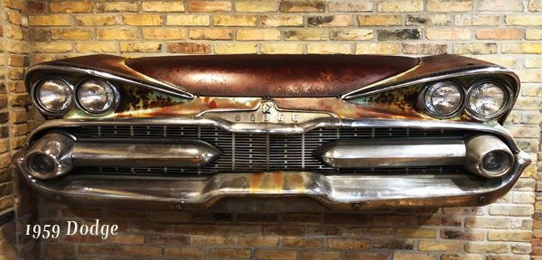 The front end of a 1959 dodge car is hanging on a brick wall.