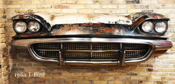 The front end of a 1960 t-bird is hanging on a brick wall.
