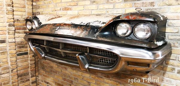 The front end of an old car is hanging on a brick wall.