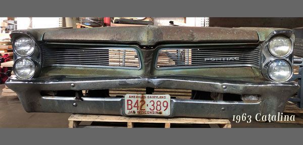 The front bumper of an old pontiac car is sitting on a wooden pallet.