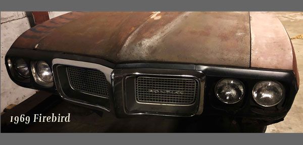 A rusty old pontiac firebird is sitting in a garage.