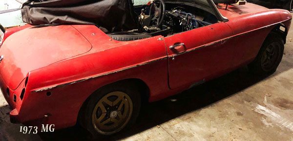 A red sports car with the top down is parked in a garage.