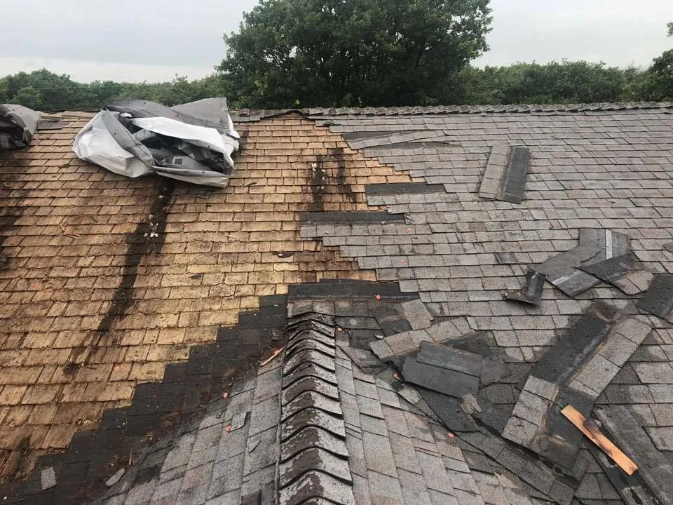 Severely damaged shingled roof with missing and torn shingles, exposing the underlayment.