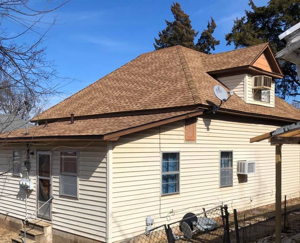 A white house with a brown roof and a satellite dish on the roof.