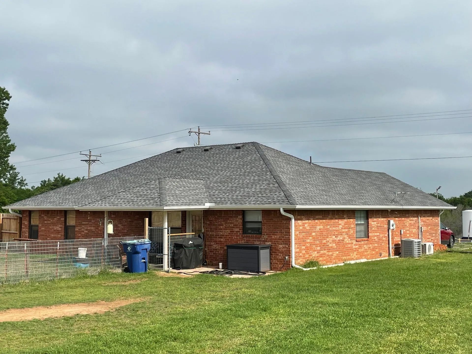Single-story brick house with gray roof and green lawn under cloudy sky
