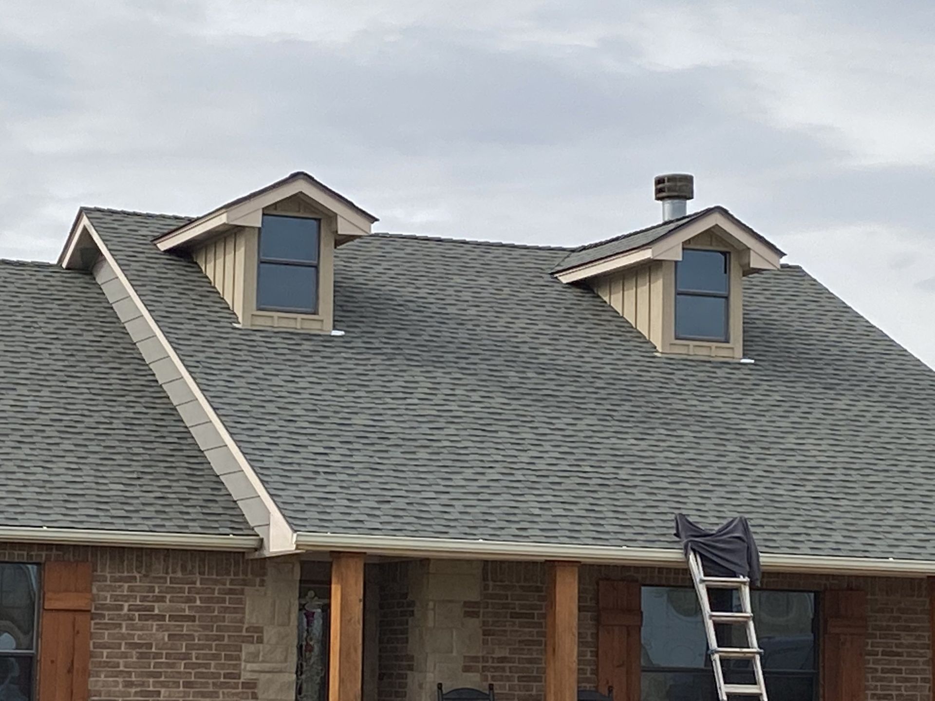 A ladder is sitting on the porch of a house with a gray roof.