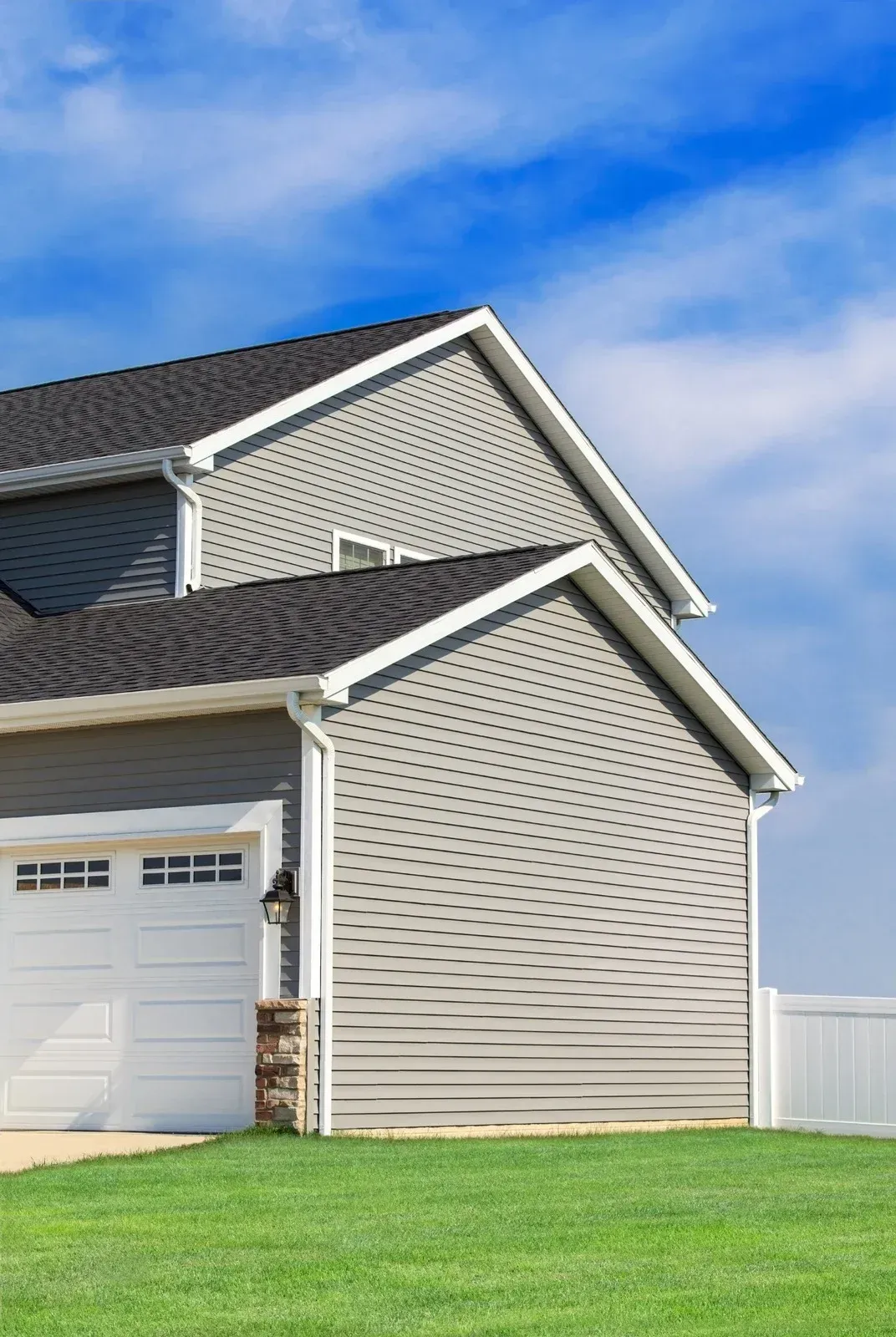 Suburban house with gray siding, garage, green lawn, and blue sky