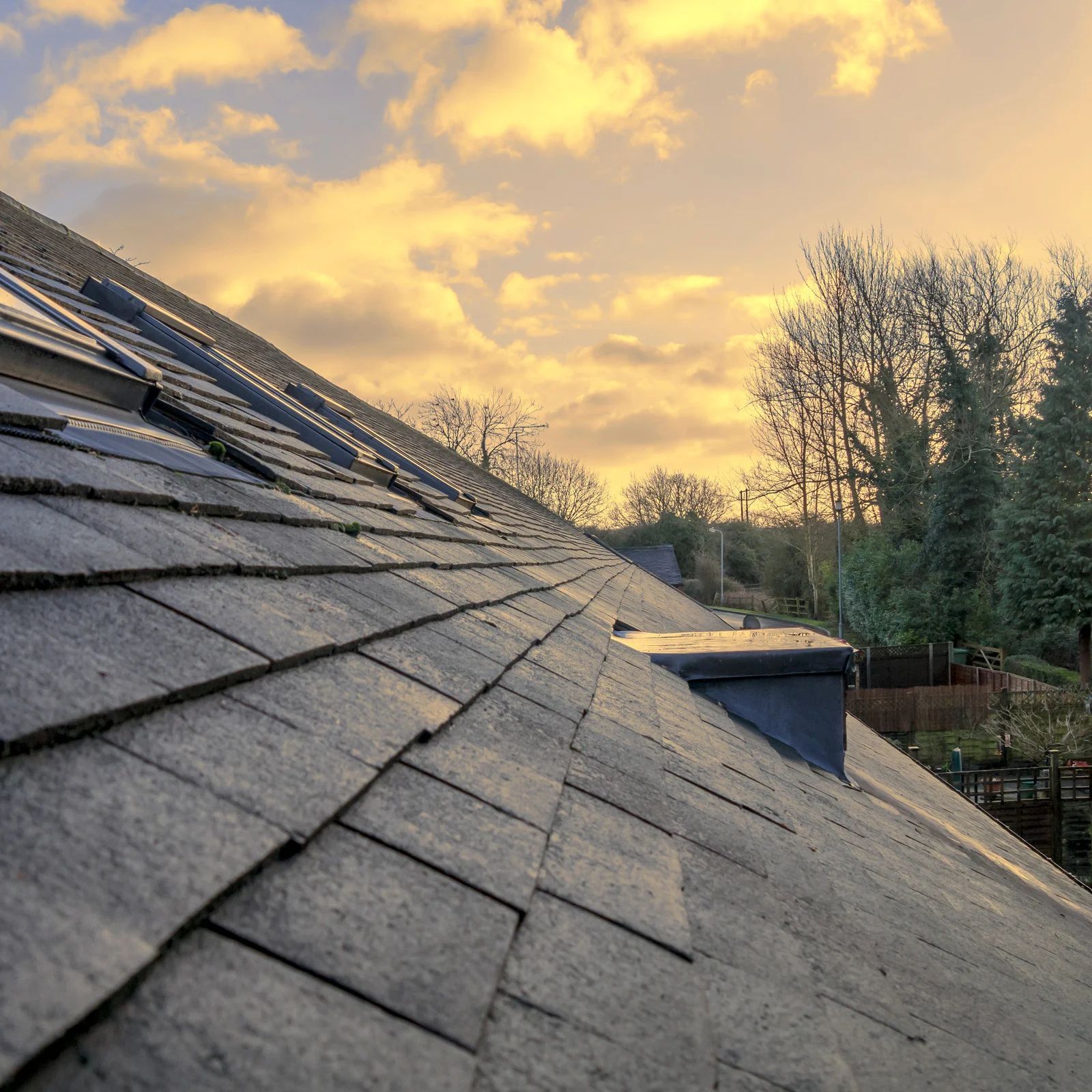 Slate roof slopes toward sunset sky with golden clouds and trees in the background