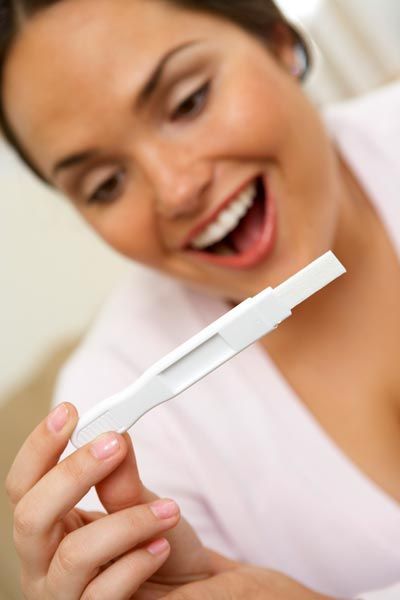 Una mujer sostiene una prueba de embarazo y sonríe