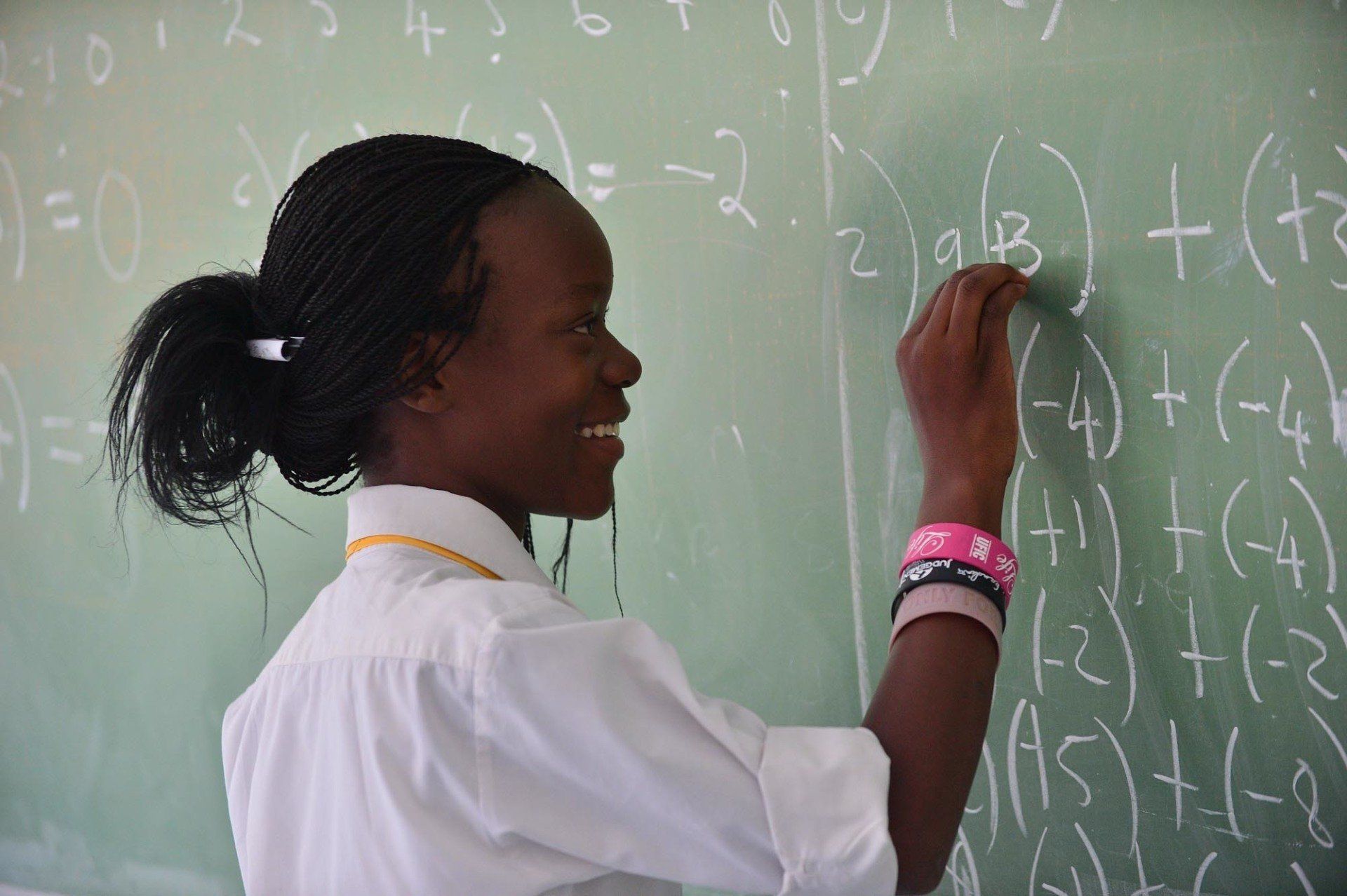 A girl is writing on a green board with chalk