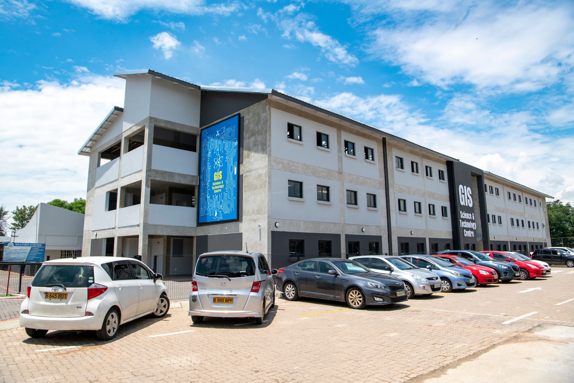 A row of cars are parked in front of a large building.