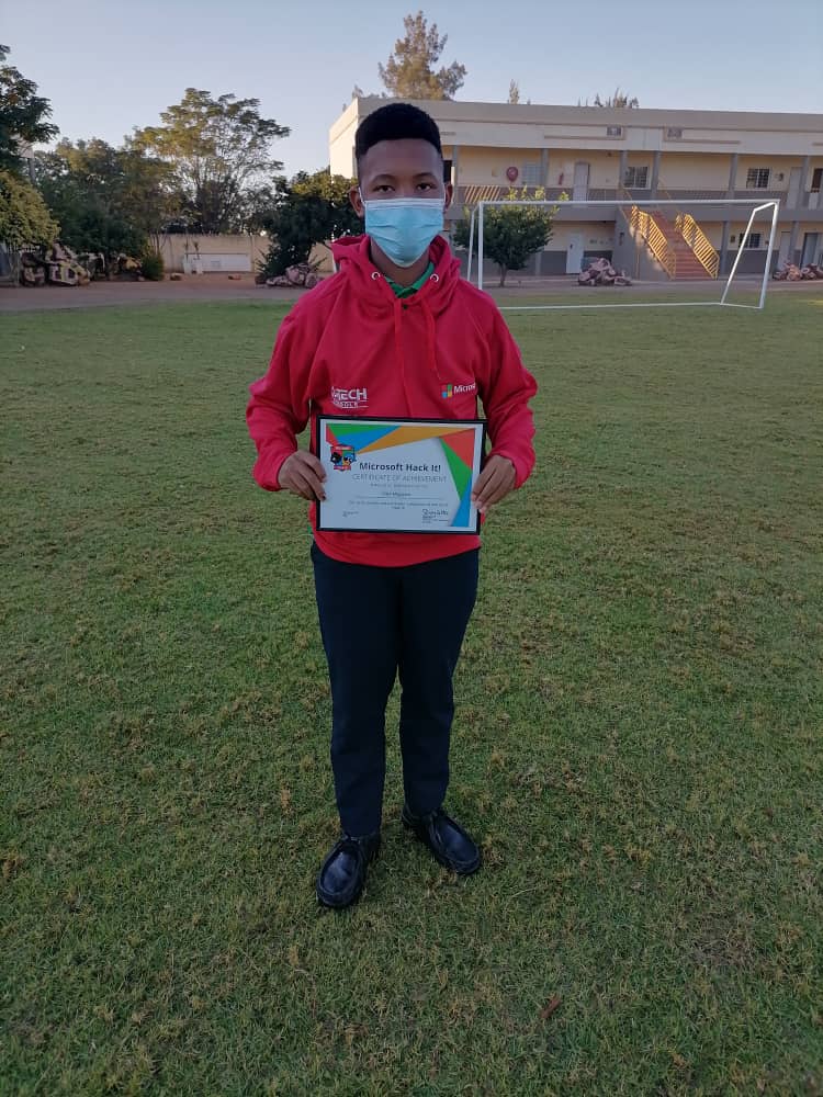 A boy wearing a mask is holding a certificate in a field.