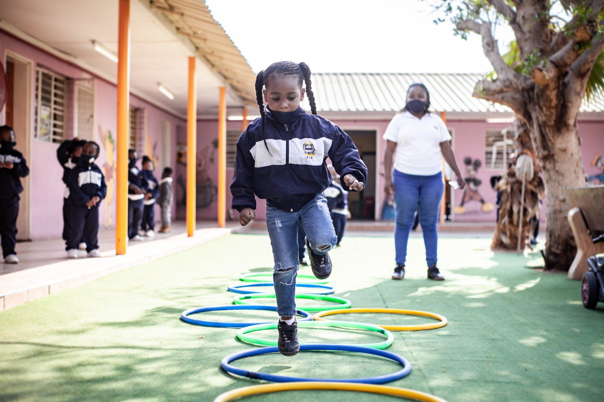A little girl is jumping through hula hoops in a school yard.