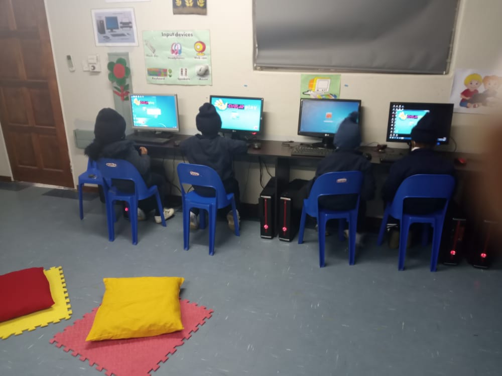 A group of children are sitting in front of computers in a room