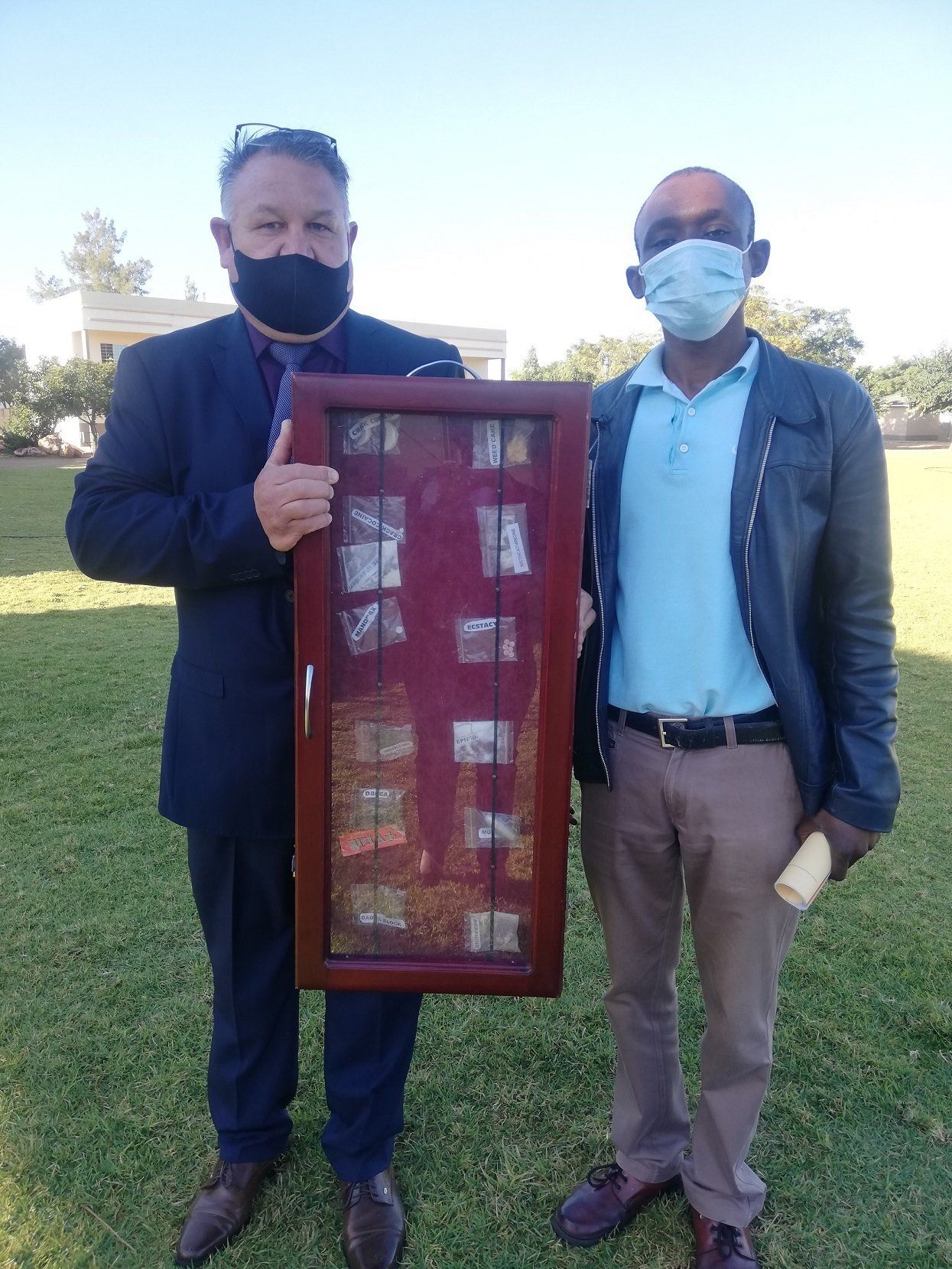 Two men wearing face masks are standing next to each other holding a display case.