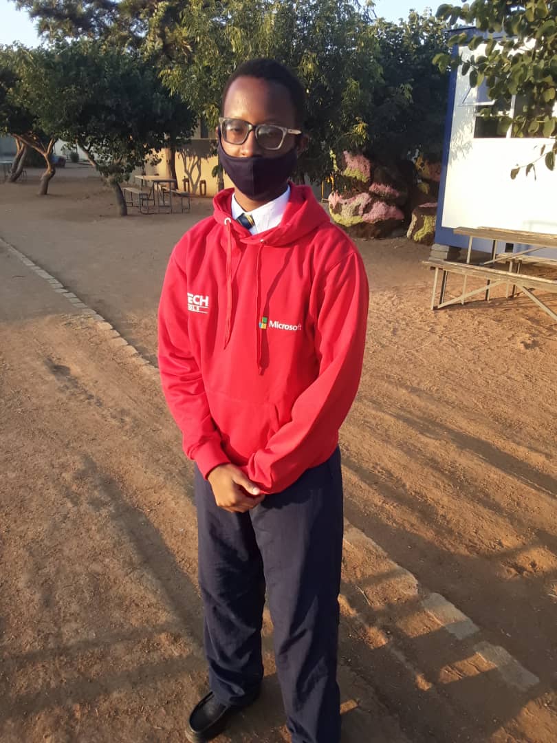 A man wearing a red hoodie and a mask is standing on a dirt road.