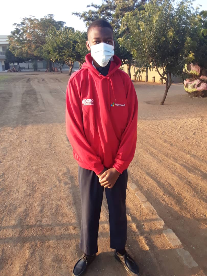 A young man wearing a mask and a red hoodie is standing in a dirt field.