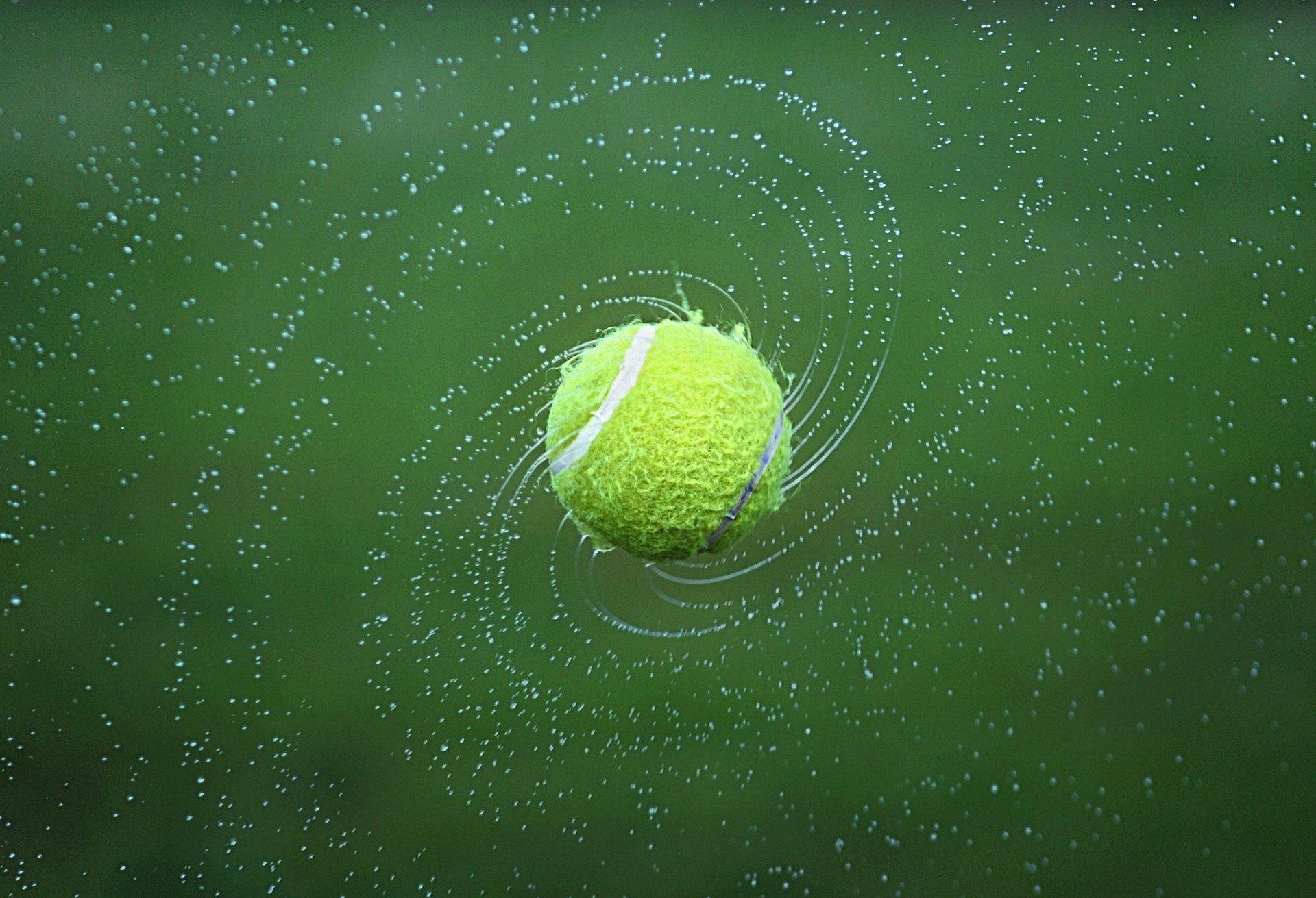 A tennis ball is spinning in the air on a green background.