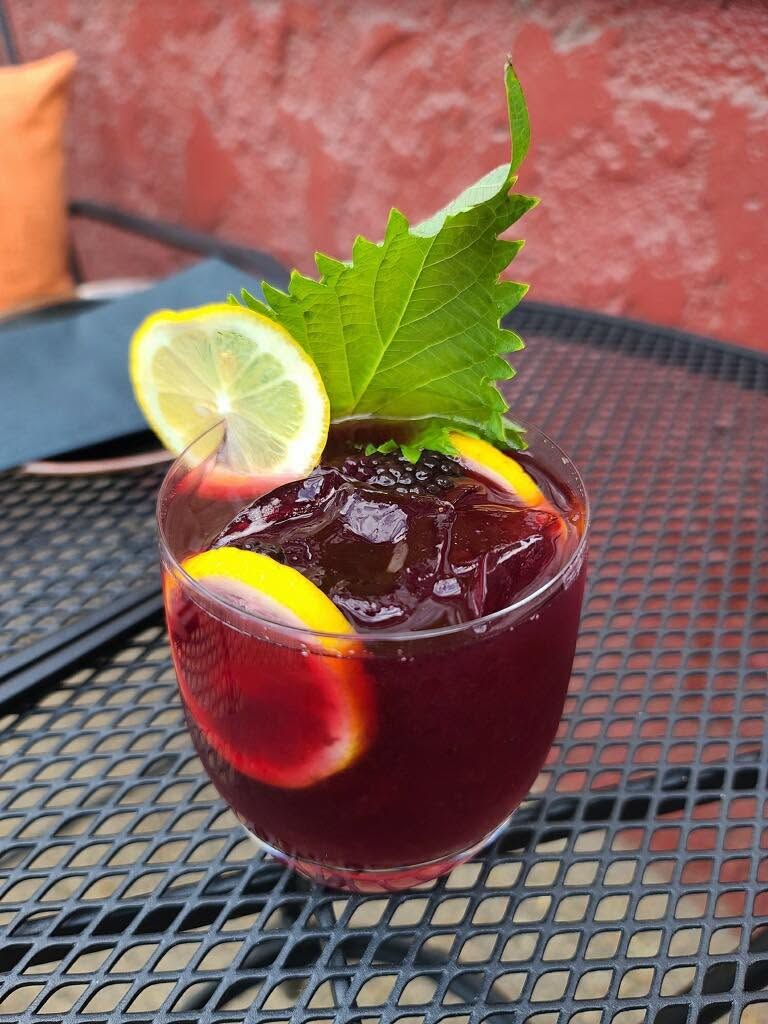 Red berry cocktail in a glass with lemon garnish and mint on a black metal table