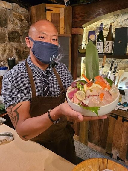 Chef holding a colorful sashimi bowl in a rustic restaurant setting