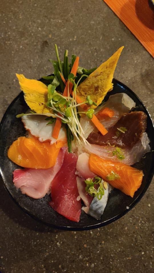 Assorted sushi sashimi arranged in a circular pattern on a black plate with garnishes.