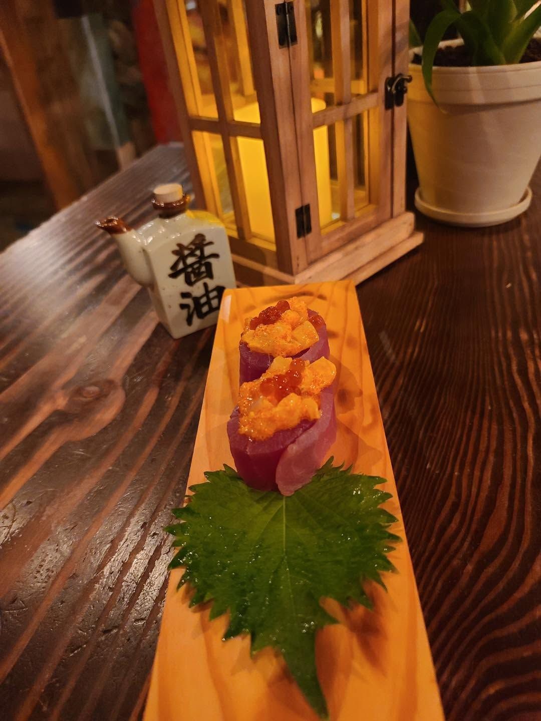 Sushi roll topped with orange fish roe and purple garnish on a wooden tray in a dim restaurant setting
