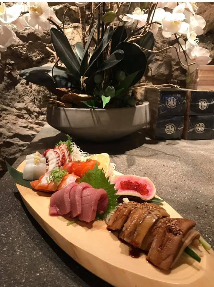 Sushi platter with assorted sashimi and rolls on a wooden board in a restaurant setting