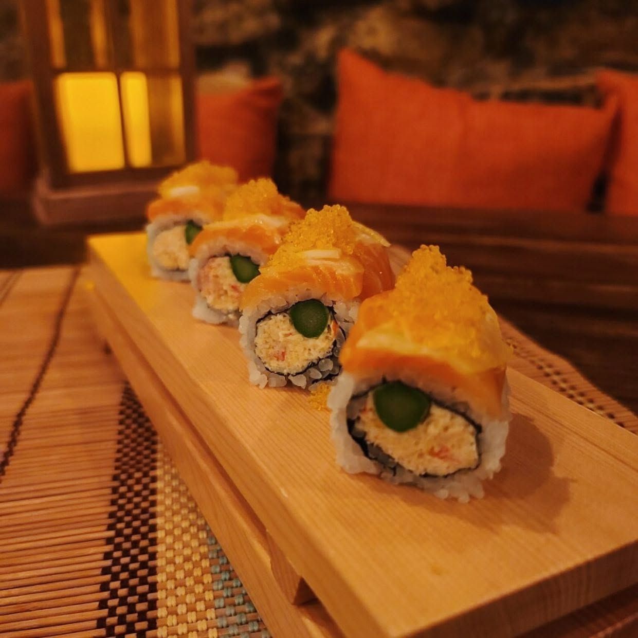 Sushi rolls on a wooden serving board in a warm-lit restaurant setting.