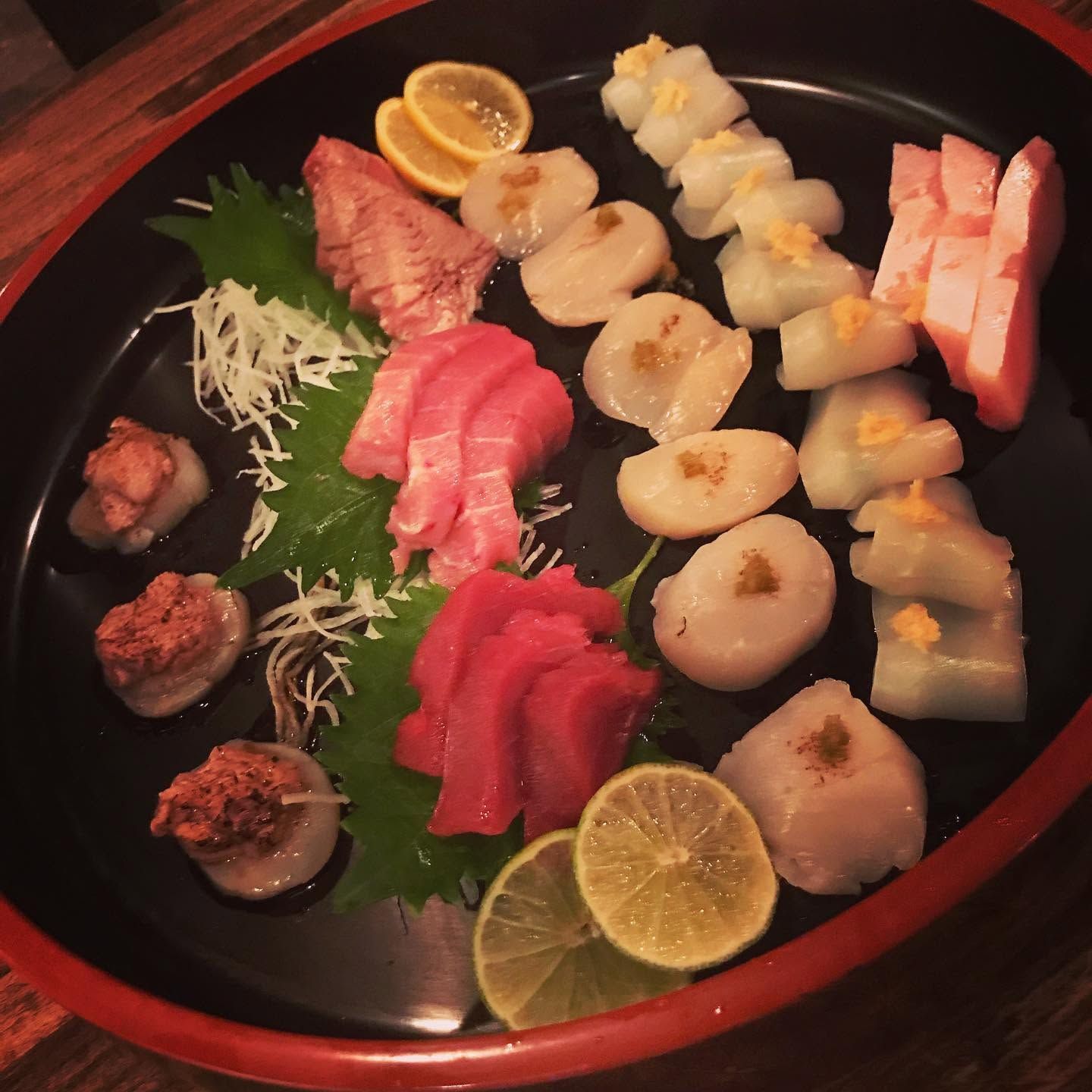 Sushi platter with nigiri, rolls, and lemon slices on a black plate with a red rim