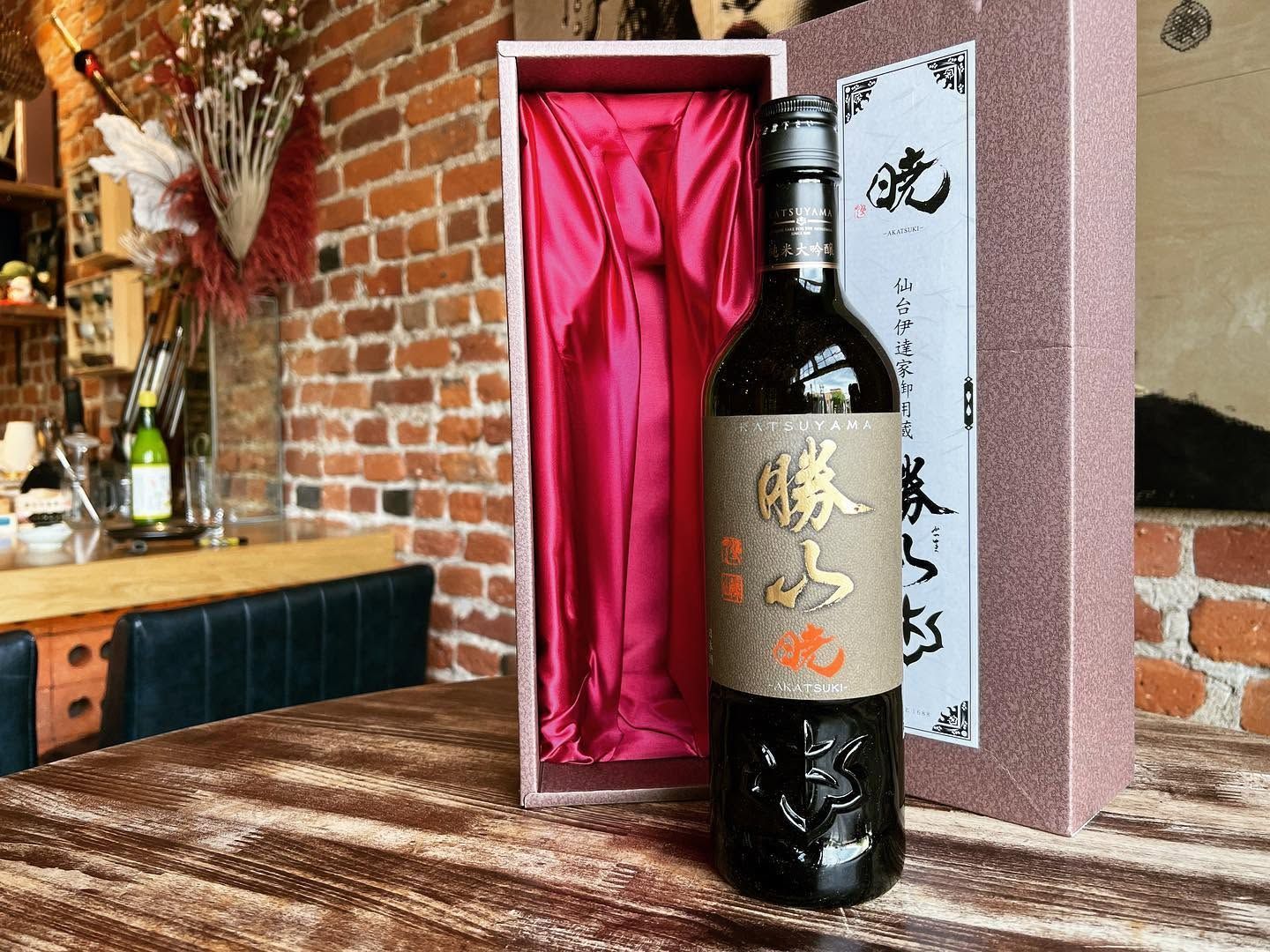Black bottle in an open red gift box on a rustic table in a brick-walled room