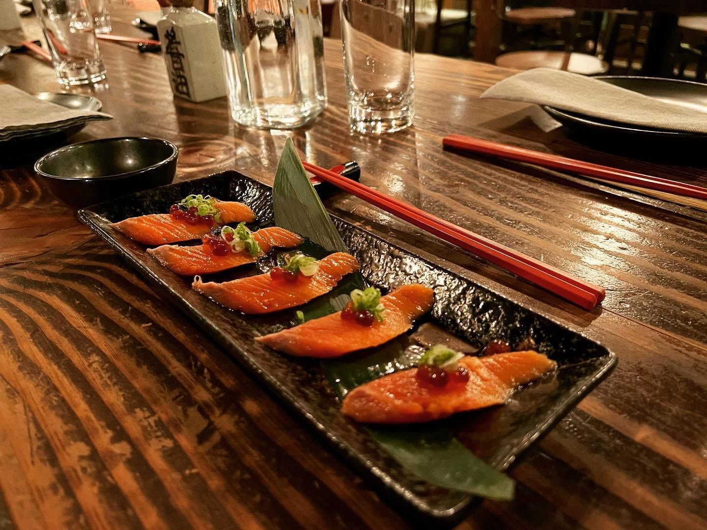Sushi appetizer platter on a wooden table with chopsticks and glasses in the background