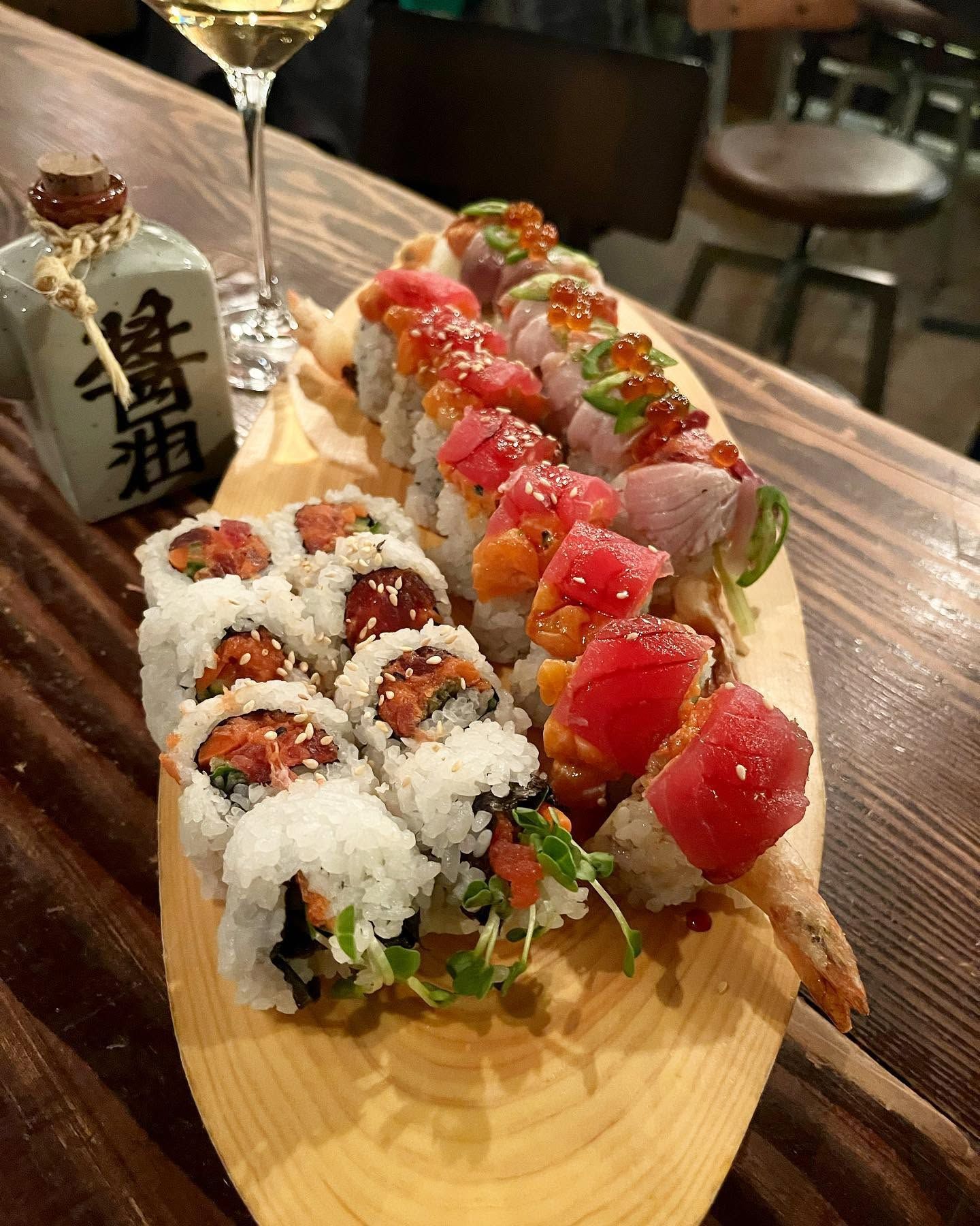 Sushi platter on a wooden board with rolls, nigiri, and a soy sauce bottle in a restaurant
