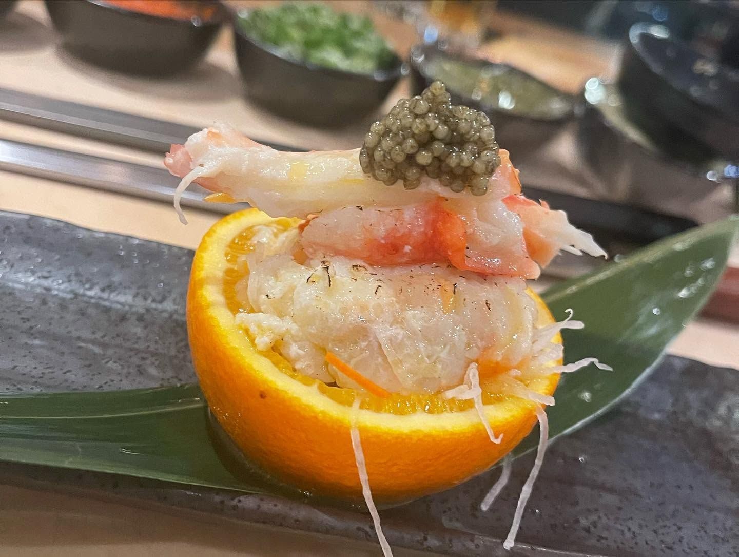 Seafood appetizer in an orange half, topped with caviar on a black plate and green leaf
