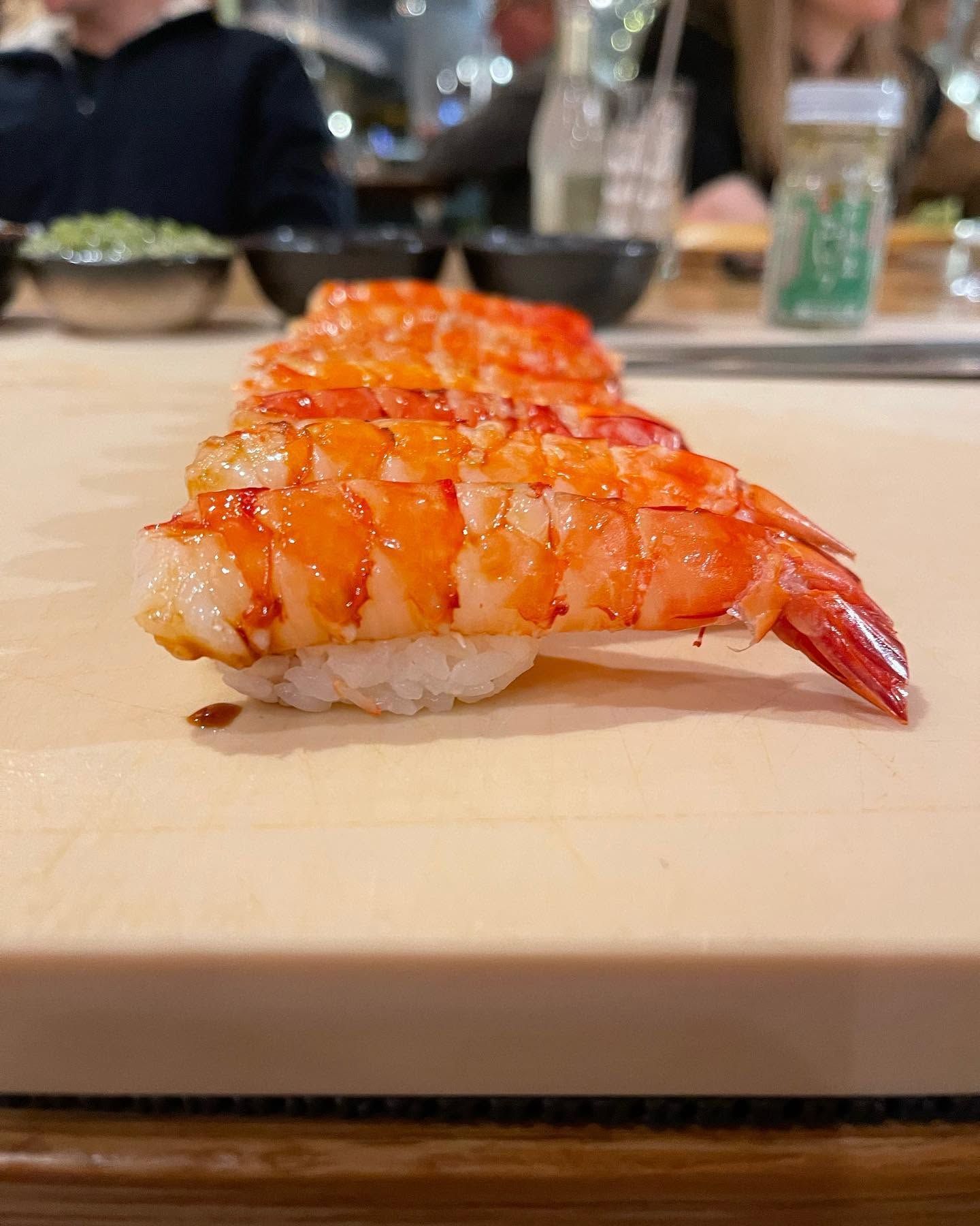 Glazed shrimp nigiri on a wooden board at a sushi restaurant counter