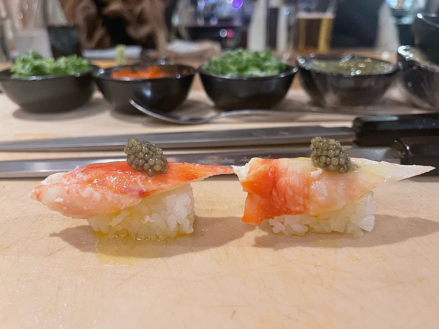Two pieces of sushi on a counter, with plates and bowls blurred in the background.