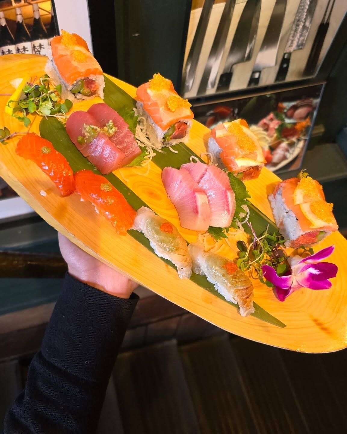 Sushi platter on a wooden board, with colorful nigiri and garnishes, held by a hand.
