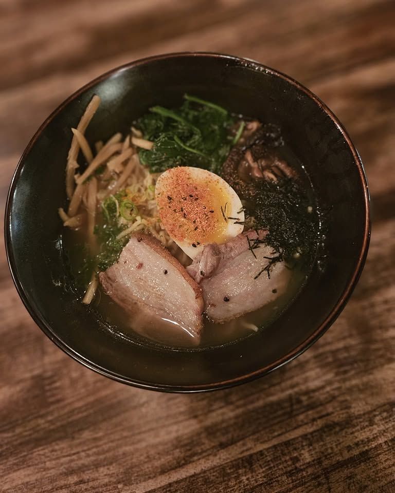 Ramen bowl with sliced pork, soft-boiled egg, seaweed, and greens on a wooden table