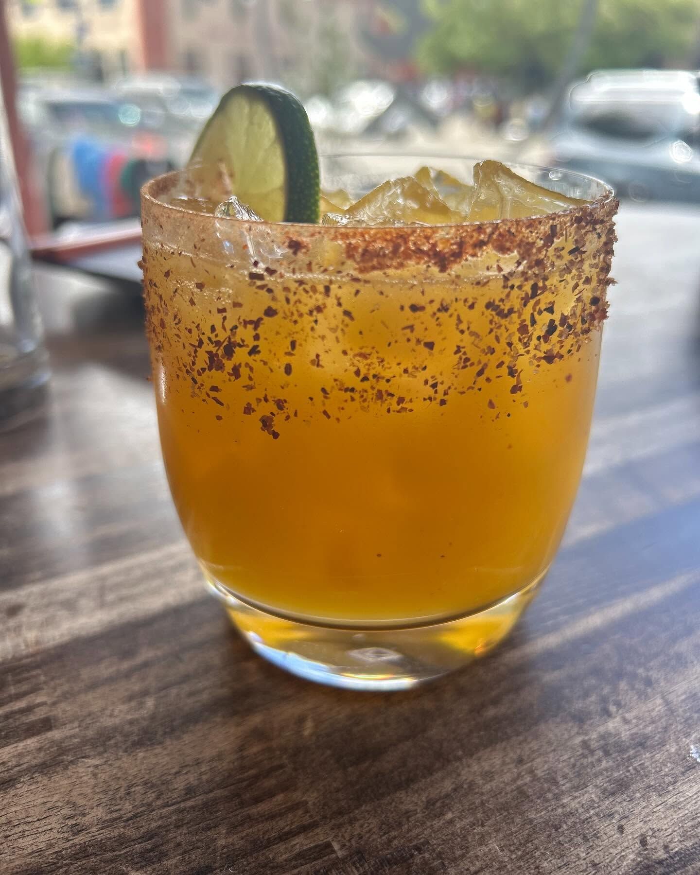 Orange cocktail in a short glass with a lime slice and chili-salt rim on a table.