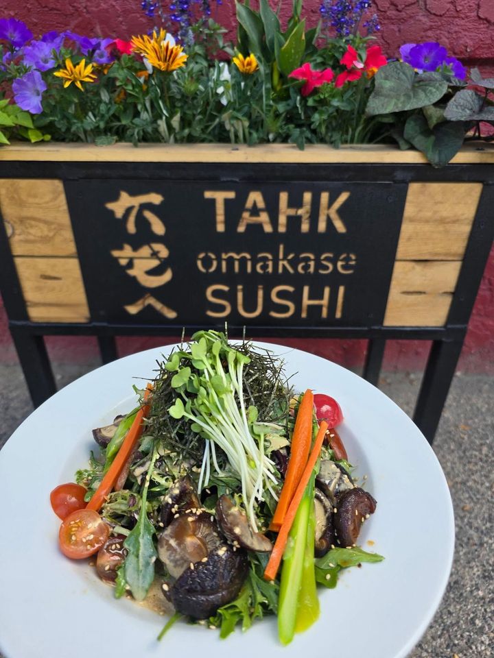 TAHK omakase sushi sign above a white plate of sushi garnished with greens and tomatoes