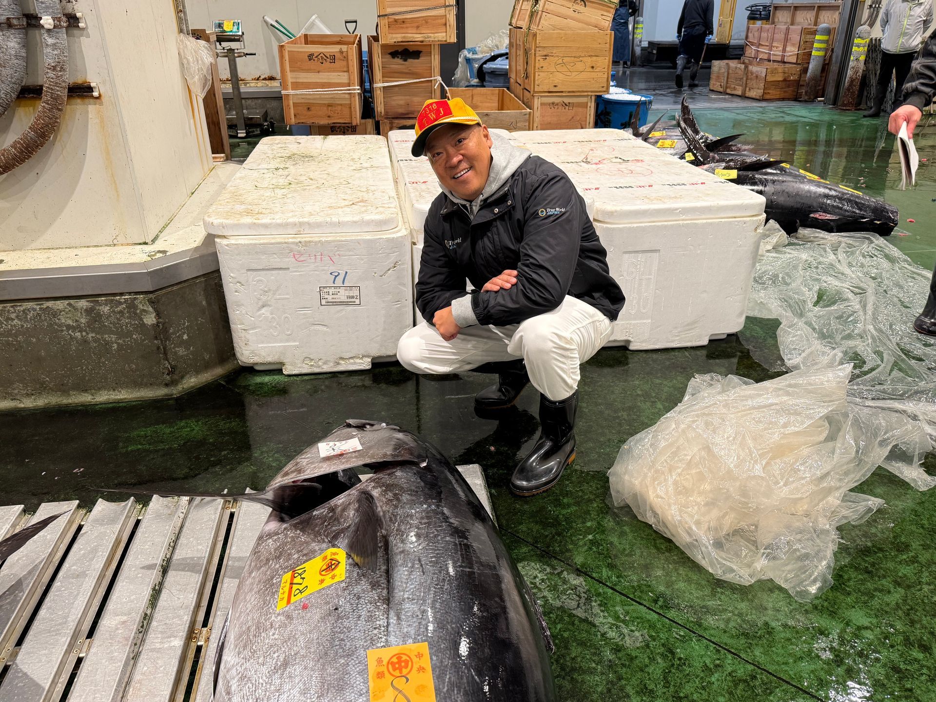 Man seated on a black boat in a warehouse, with fish boxes and packing materials nearby.
