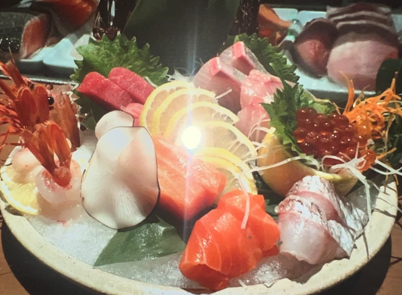 Assorted sashimi and sushi pieces arranged on a black platter with lemon slices and garnish