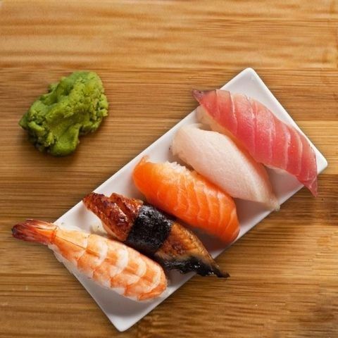 Sushi platter with wasabi on a wooden table, featuring assorted nigiri on a rectangular white plate