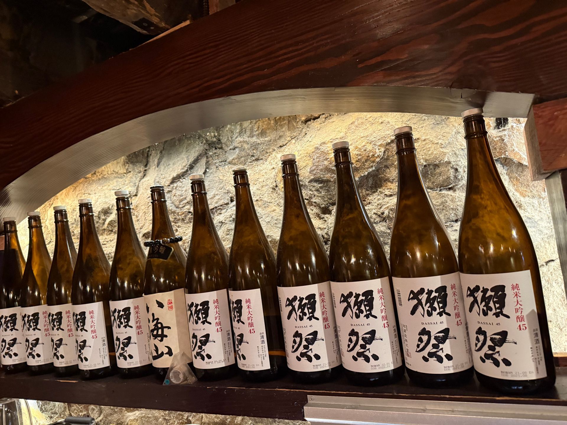 Row of Japanese sake bottles with white labels on a wooden shelf in a bar