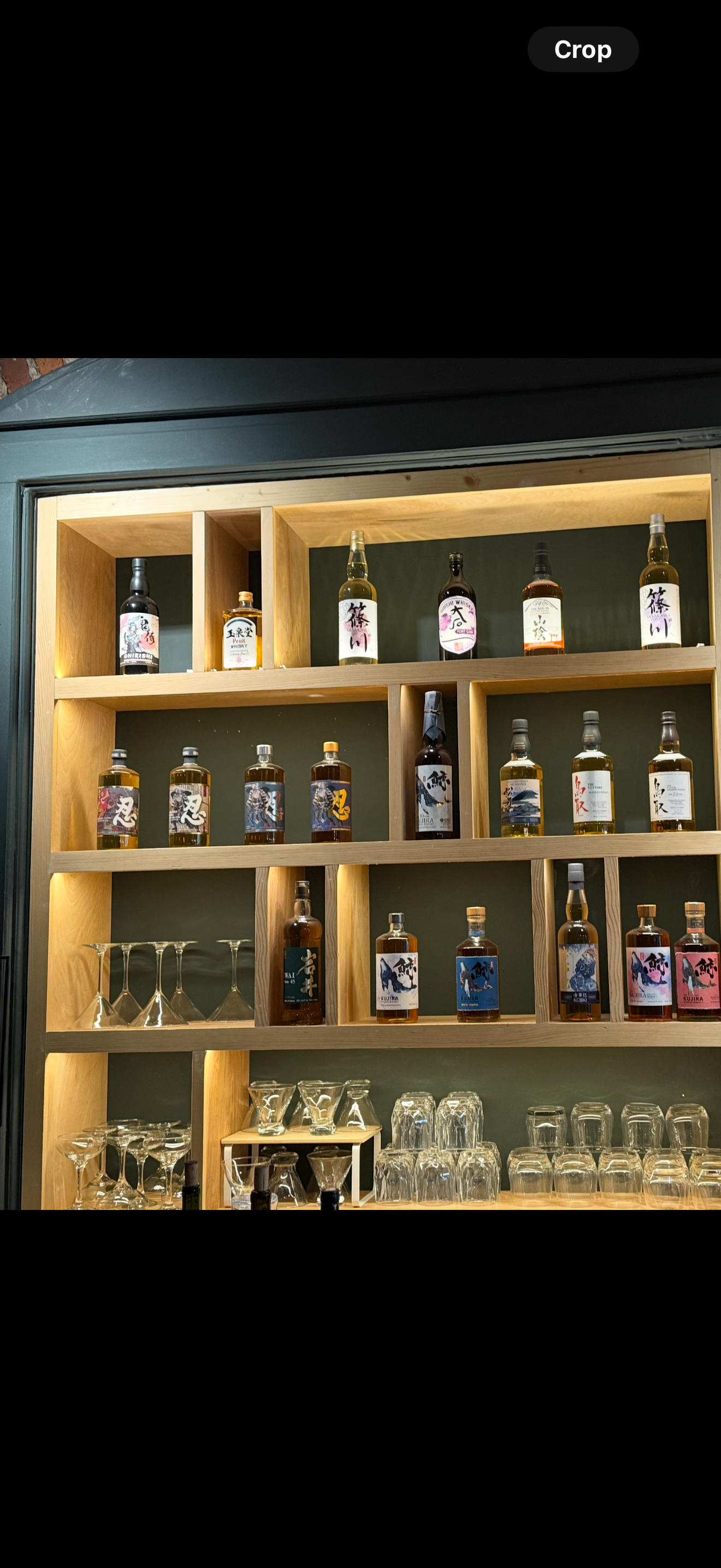 Wooden shelf of liquor bottles and glassware in a warmly lit bar display