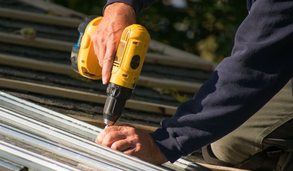 A Man is Working on a Roof With a Drill — Cairns Roofing Contractors Pty Ltd in Bungalow, QLD